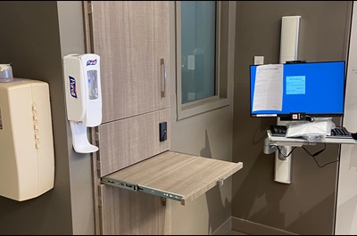 In a hallway on a patient floor in the Pavilion, a nurse’s touch down station includes two computer monitors and, to the right of the station, a tall vertical storage cabinet with large upper and lower doors and a smaller door with a lock in the center.